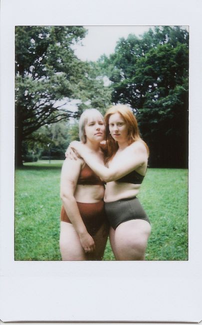 Two women in swimsuits embrace in a lush green park setting, exuding a sense of friendship.