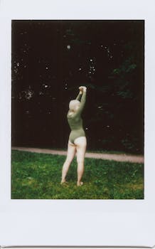 花园里，一名身穿绿色紧身衣的女子正举起双臂站着