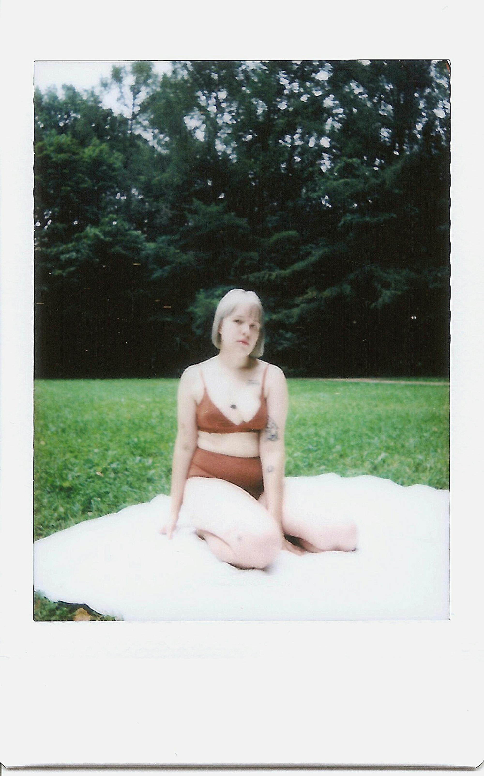 Blonde woman in a minimalist portrait sitting outdoors on grass during summer.