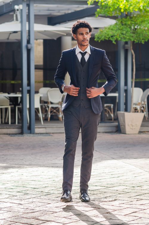 Free Confident man in a formal black suit walking on a sunlit pavement in a city. Stock Photo