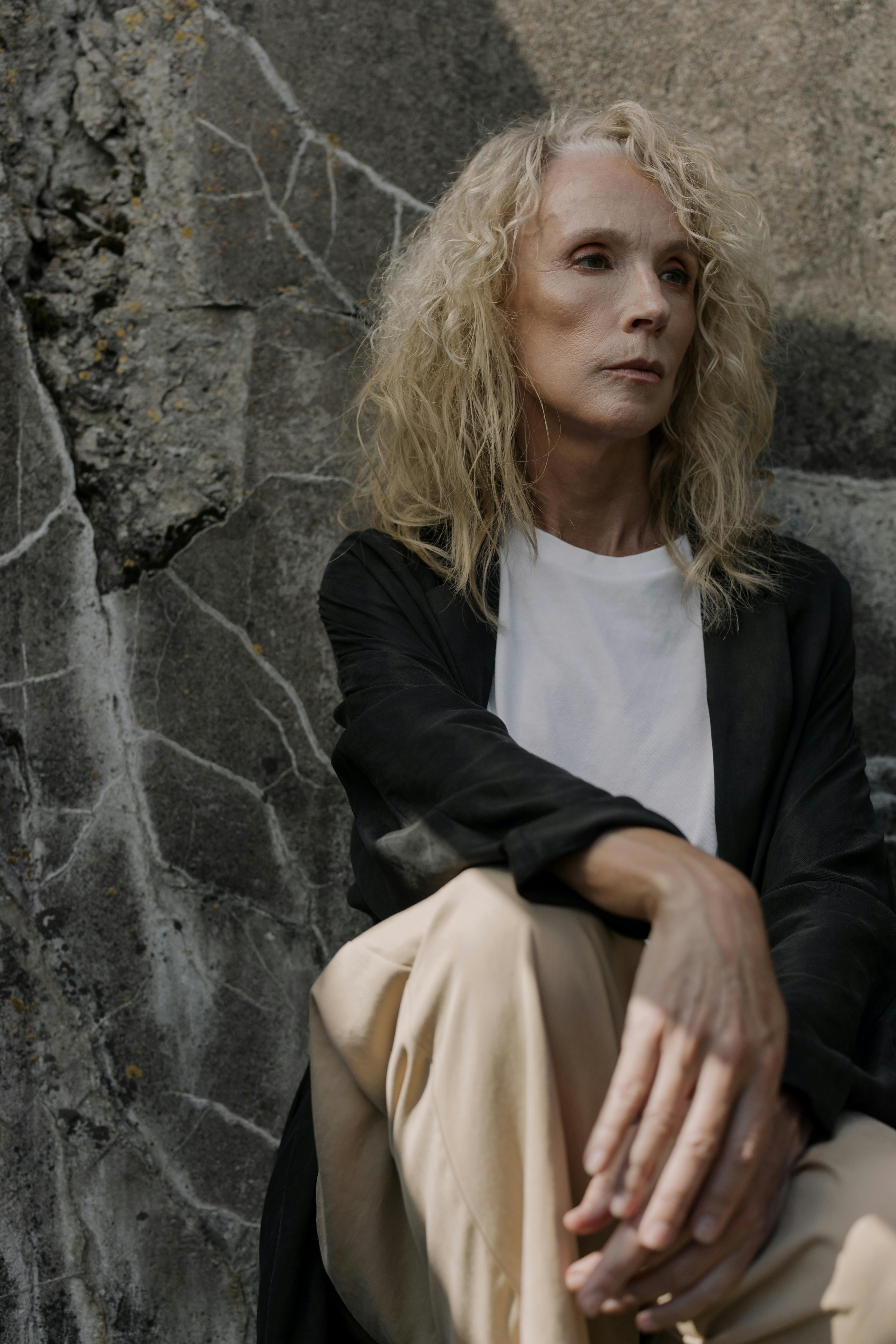 woman in black cardigan leaning on gray concrete wall