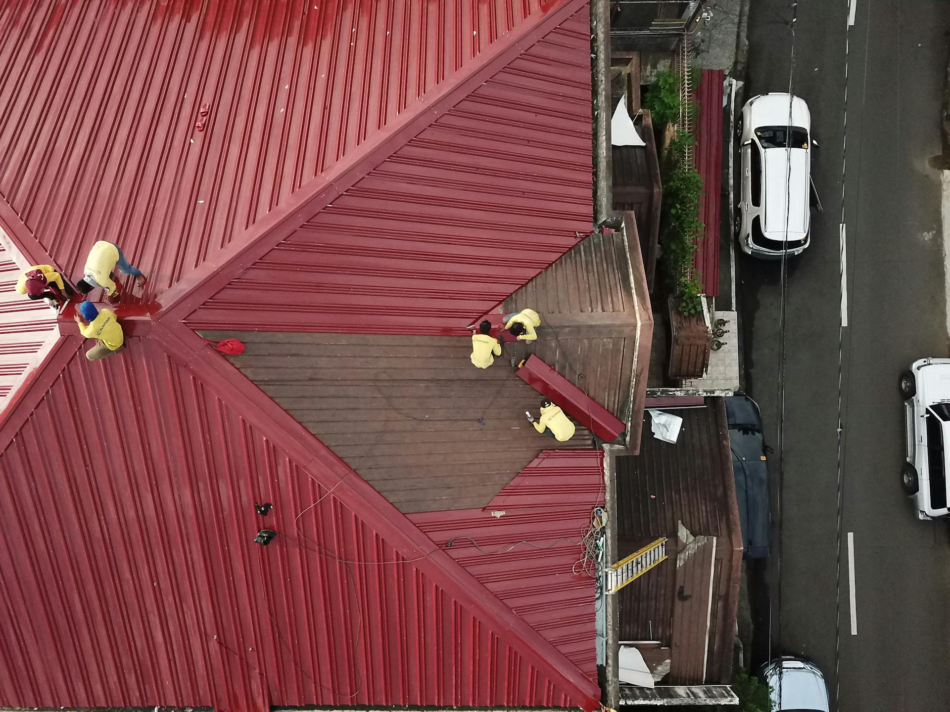 Aerial view of workers repairing a red metal roof in Quezon City, Philippines.