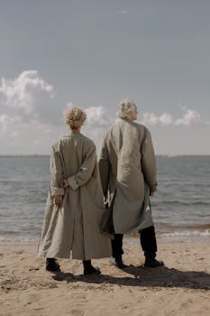 一对老夫妇穿着长外套，并肩站在沙滩上，留下背影