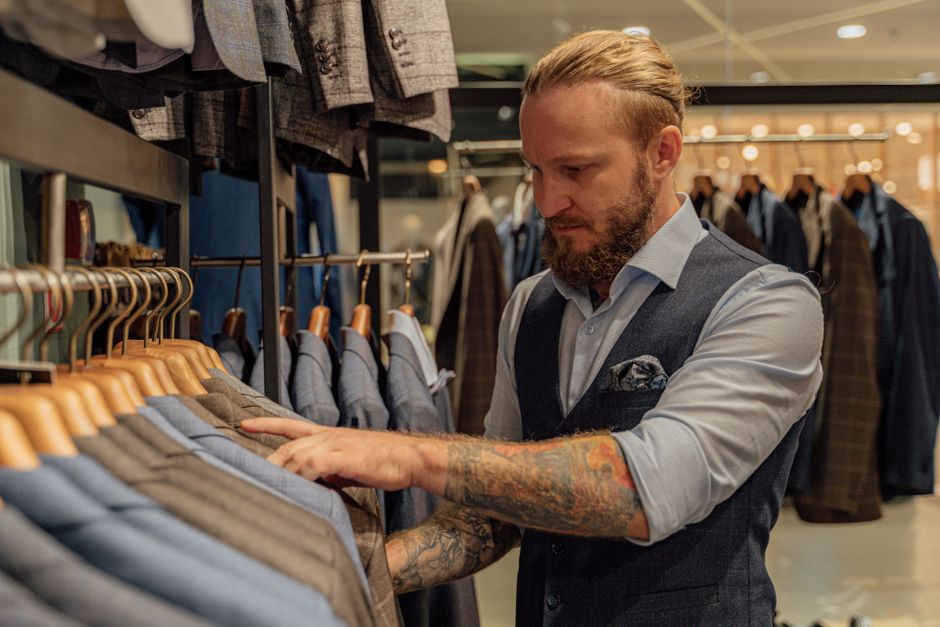 Tattooed man selecting suits in a fashionable clothing store, elegant setting. Tattooed man selecting suits in a fashionable clothing store, elegant setting.