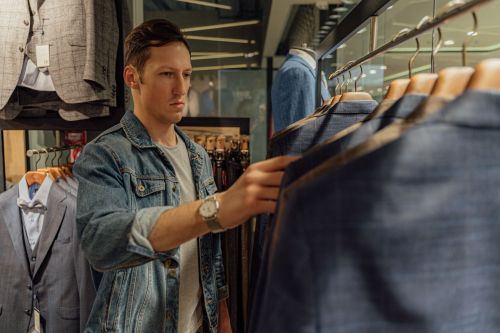 Free Young man browsing through suits in a retail clothing store, selecting new attire. Stock Photo