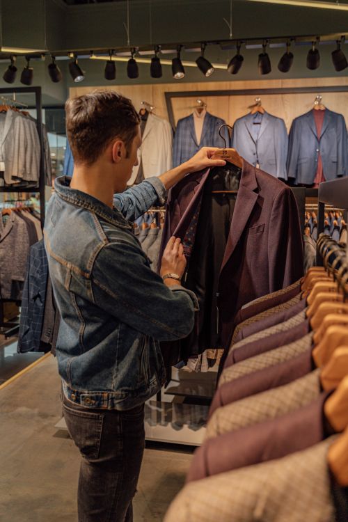 Free A man browsing through suits in a stylish clothing store, examining a jacket. Stock Photo
