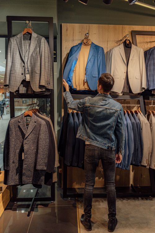 Free A man examines suits in a stylish fashion store display, highlighting modern shopping choices. Stock Photo