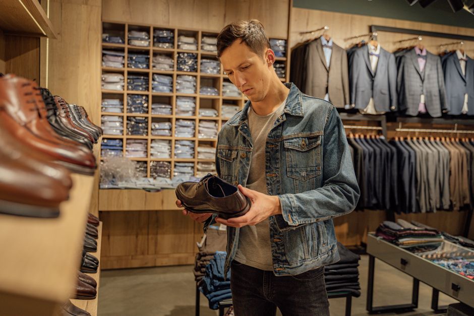 A young man inspects leather shoes in a stylish boutique's menswear section. A young man inspects leather shoes in a stylish boutique's menswear section.