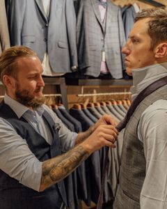 Professional tailor adjusts customer's necktie in a stylish men's suit store.