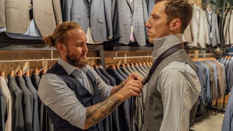 Professional tailor adjusts customer's necktie in a stylish men's suit store.