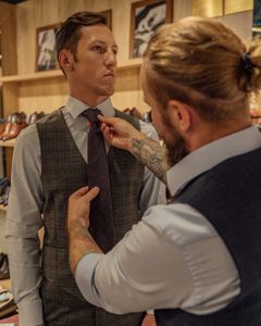A tailor assists a client by adjusting his necktie in a clothing store fitting session.