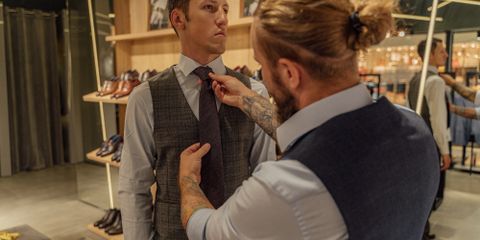 A tailor assists a client by adjusting his necktie in a clothing store fitting session.