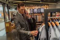 一位时尚男士正在一家现代服装店里一边浏览西装，一边打电话