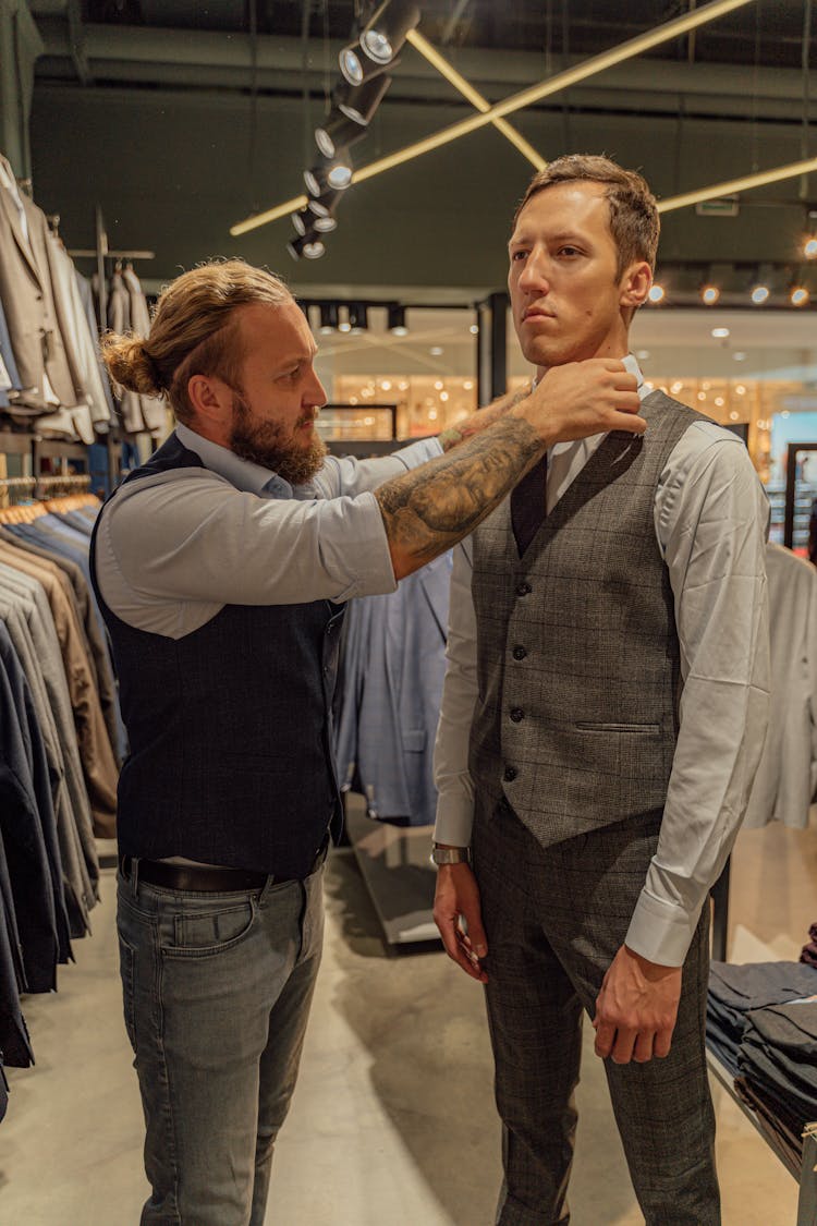 A Salesman Helping A Male Customer Fit A Plaid Vest