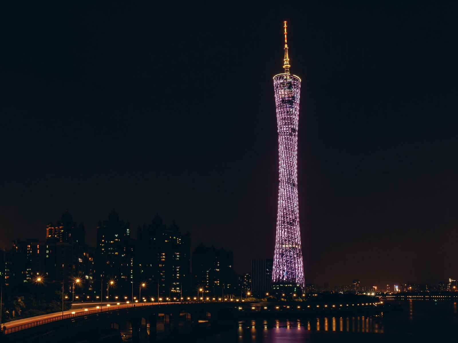The Canton Tower rising above the Pearl River at night, the city's lights mirrored on the water