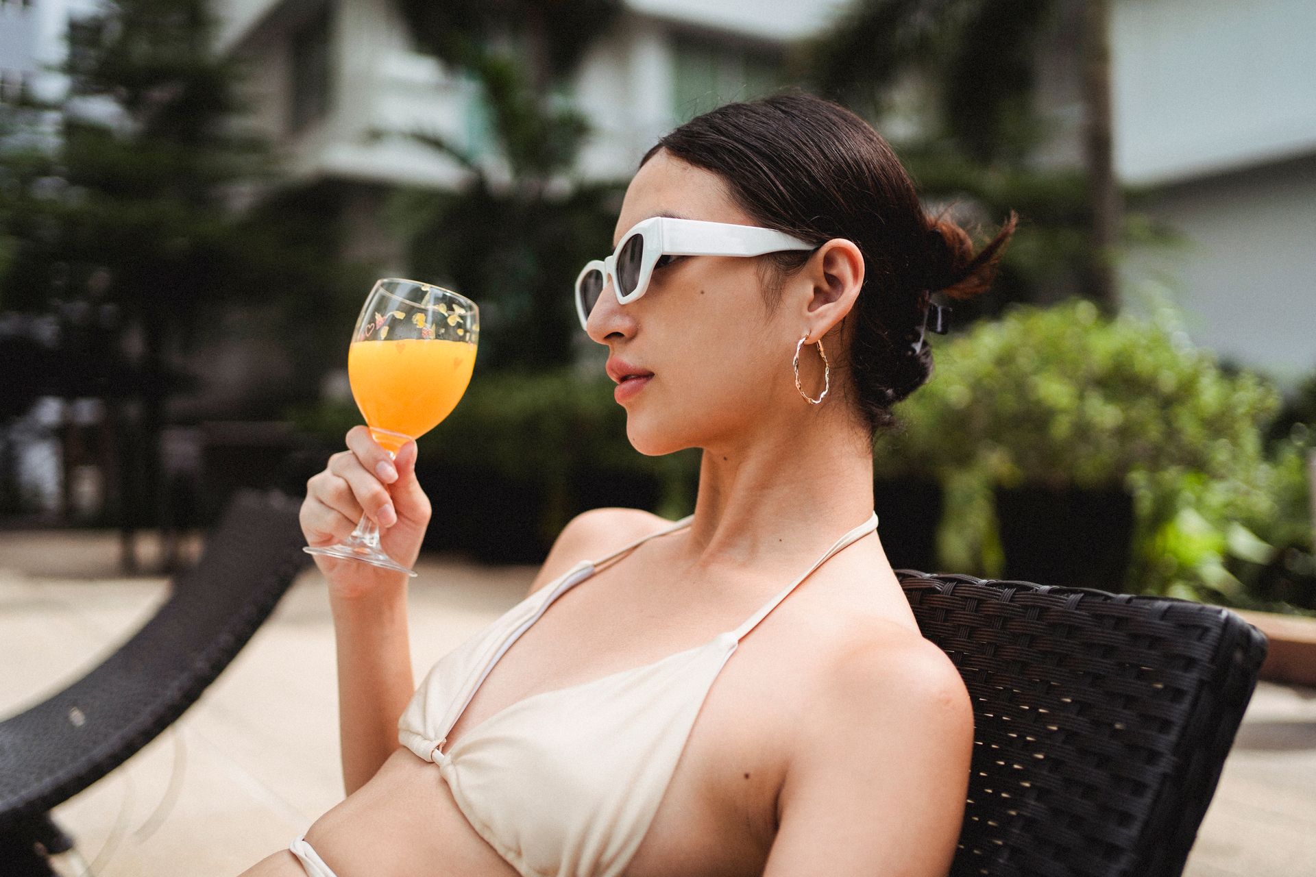 Stylish young ethnic woman drinking smoothie while chilling on sunbed in resort