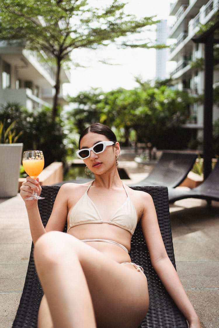 Confident Young Ethnic Lady Drinking Juice Lying On Sunbed At Poolside