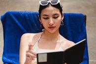 一名年轻女子穿着泳衣，在泳池边看书，享受着户外阳光明媚的一天