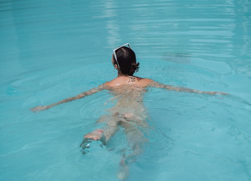 Free Back view of unrecognizable lady with dark hair in bikini and sunglasses on head swimming in clean pool on sunny summer day Stock Photo