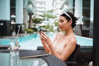 年轻女子在豪华度假村阳光明媚的一天，于泳池边在线连接