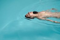 Content young female in beige bikini swimming with eyes closed in swimming pool and enjoying warm sun rays