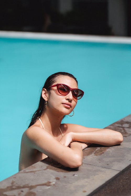 Charming woman in stylish sunglasses leaning on pool edge