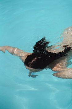 High angle unrecognizable brunette swimming underwater in clean blue pool water on sunny day