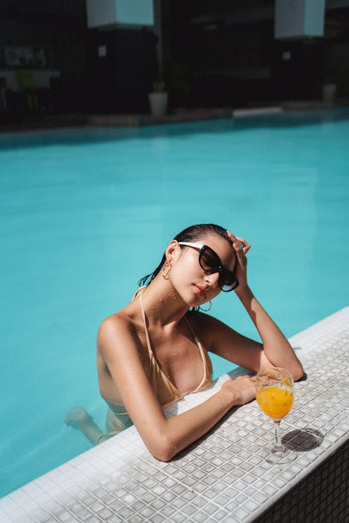 Beautiful tanned woman chilling in swimming pool with orange juice