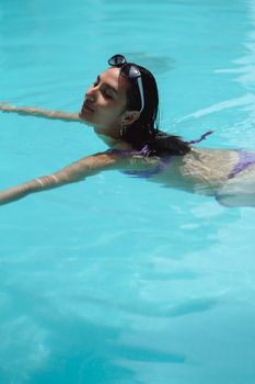 Side view content relaxed female in stylish sunglasses swimming in blue pool water on sunny day