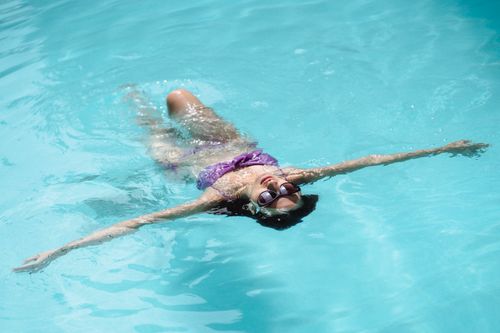Free High angle slim attractive female in purple swimwear and trendy sunglasses floating on back in pool on sunny weather Stock Photo