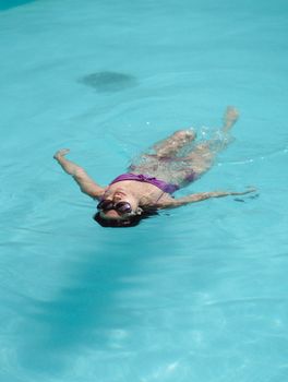 From above full length beautiful fit brunette floating on back in swimming pool on sunny weather