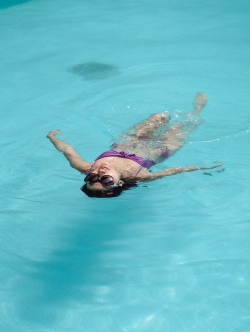 Free From above full length beautiful fit brunette floating on back in swimming pool on sunny weather Stock Photo