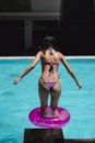 阳光明媚的日子里，一位苗条女性穿着比基尼、戴着橡皮圈，在室外游泳池游泳前，面目全非的背影