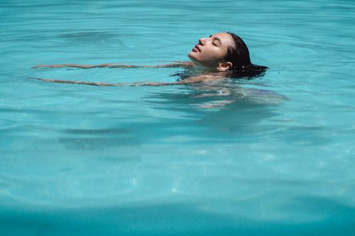 Free Side view of young ethnic lady with dark wet hair swimming in blue water of pool with closed eyes on sunny day Stock Photo