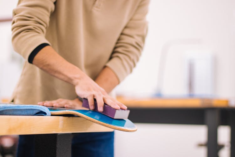 A Person In Brown Sweater Wiping The Blue Wooden Board On The Table