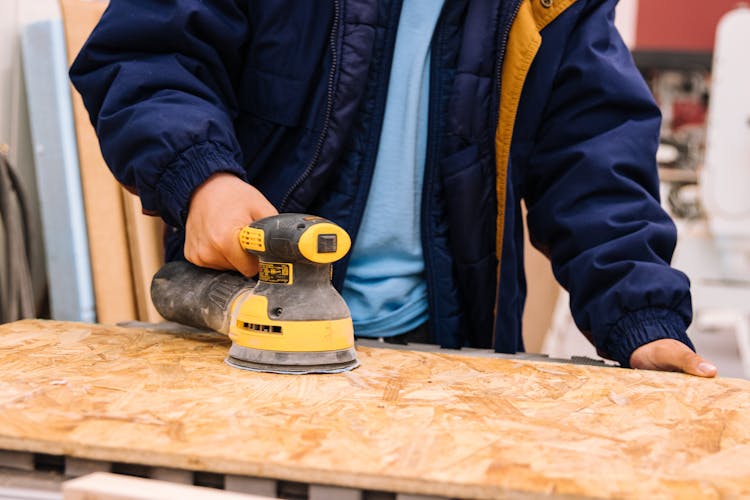 Person In Blue Jacket Using A Power Tool On Wooden Board