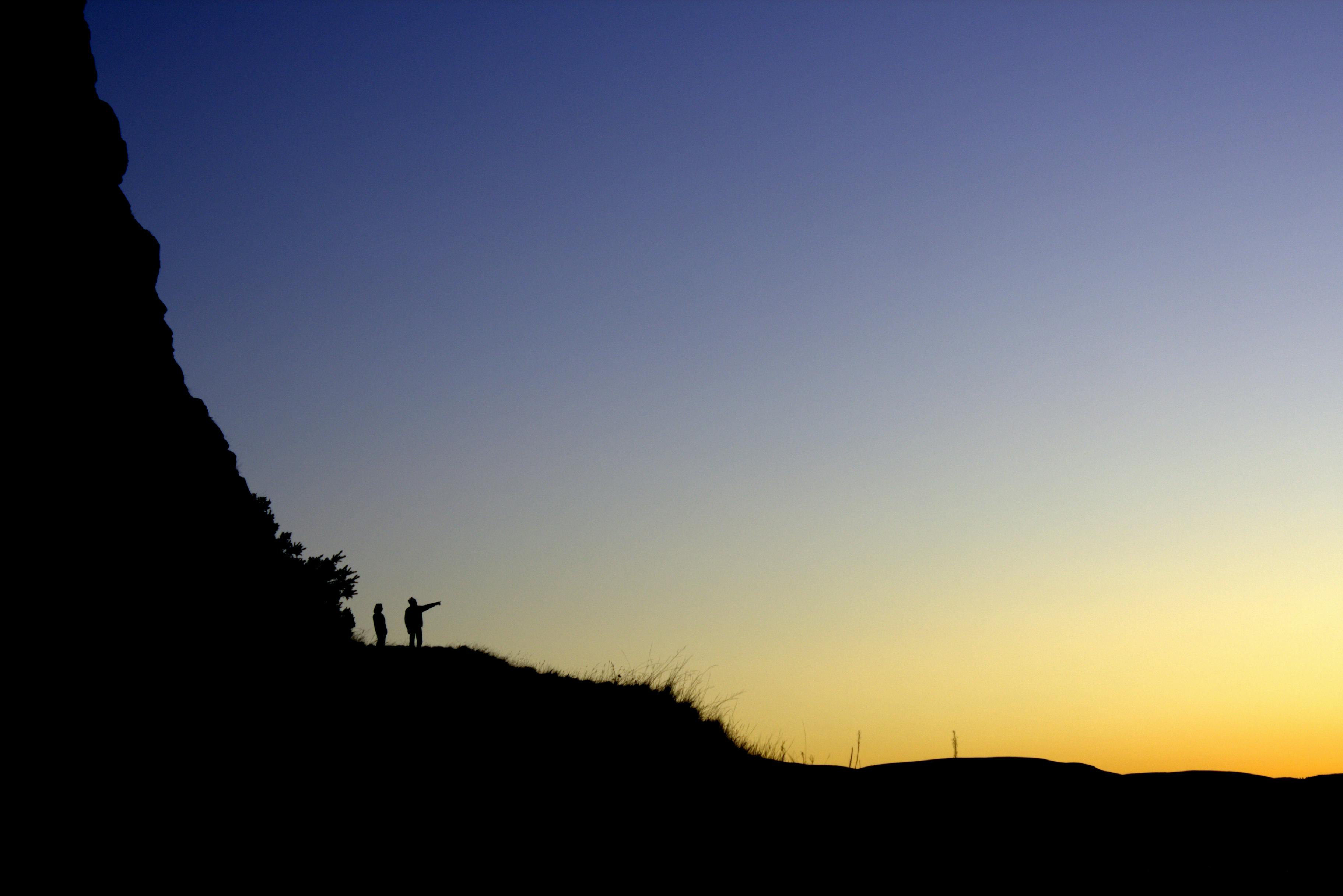 Silhouettes of hikers on a hill during a vibrant sunset in the Scottish Highlands.