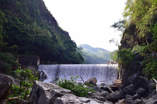 瀑布从岩石悬崖间的沟壑中倾泻而下，阳光明媚，绿树生长，景色令人惊叹