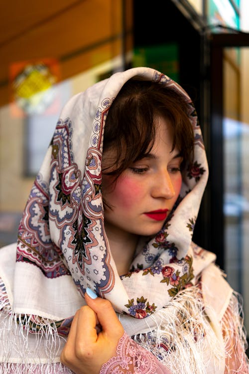 Free Side view of beautiful female in traditional headscarf with blush on cheeks looking away while standing on street near blurred building Stock Photo