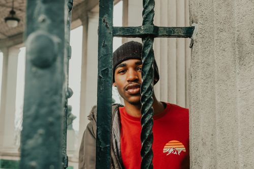 Free Young man in a red shirt stands behind a decorative iron gate outdoors. Stock Photo