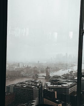 Aerial view of London's skyline shrouded in mist, featuring Tower Bridge and the River Thames.