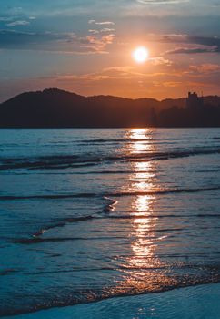 Tranquil ocean waves with a stunning sunset behind silhouetted mountains for a peaceful evening view.