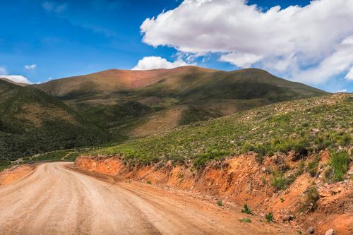 Free Explore a winding dirt road leading through lush green mountains under a bright blue sky. Stock Photo