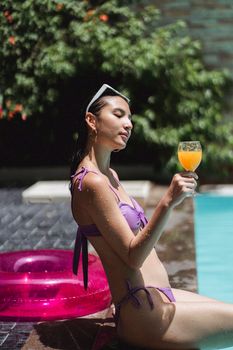 Side view of female tourist wearing bikini while drinking fresh juice on poolside in summer day