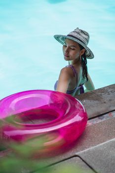 High angle back view of young female wearing swimsuit and hat enjoying vacation in blue swimming pool