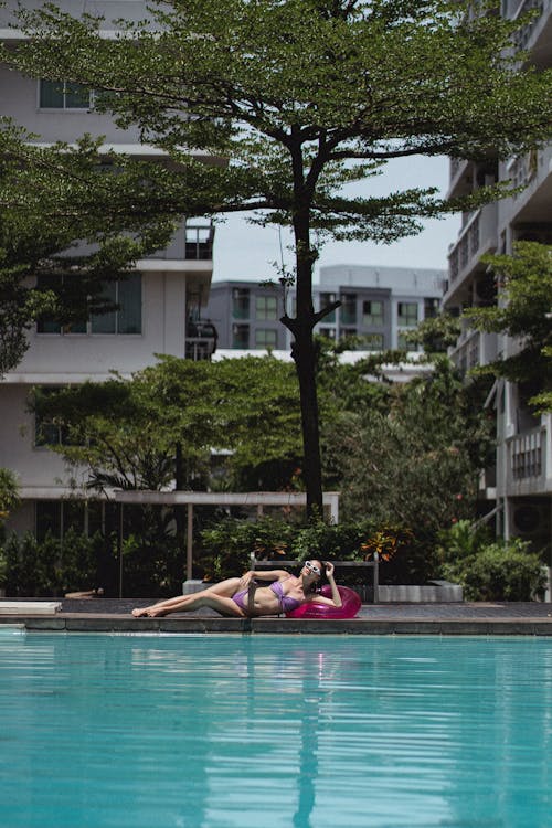 Full body of barefoot female traveler wearing bikini relaxing on poolside near swimming pool with blue water