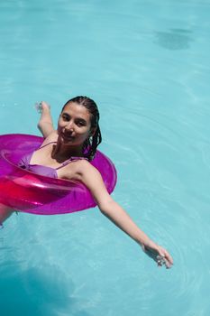 From above of calm young female wearing swimwear floating in blue water of pool with arms outstretched