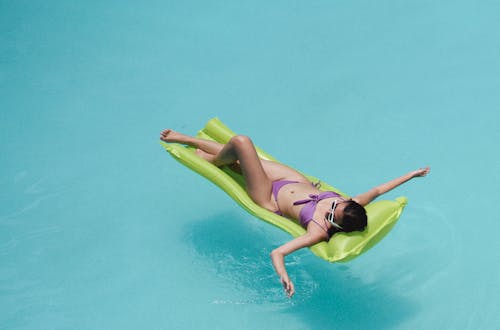 Женщина в купальниках, загорая на надувном матрасе в бассейне
