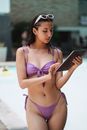 Attractive young lady wearing stylish swimwear and white sunglasses surfing internet on tablet while standing near poolside