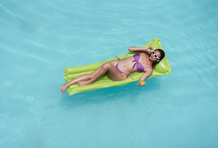 Relaxed Woman Sunbathing On Air Mattress In Swimming Pool